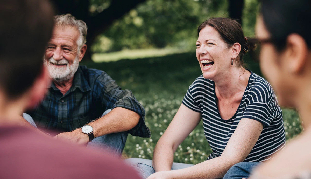 A group of people laughing together while sitting outside in a circle.
