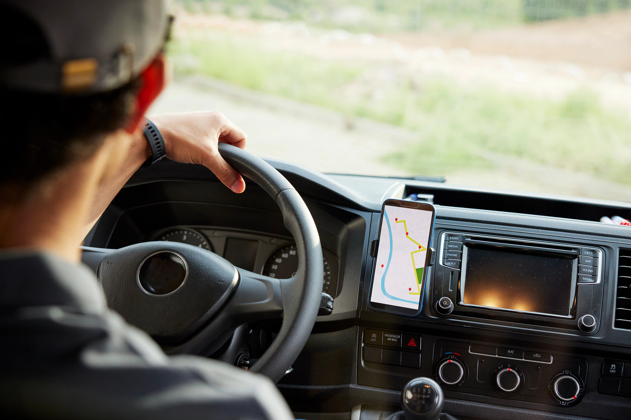 a smartphone with mapped point on the screen in a phone holder next to a person driving in a car