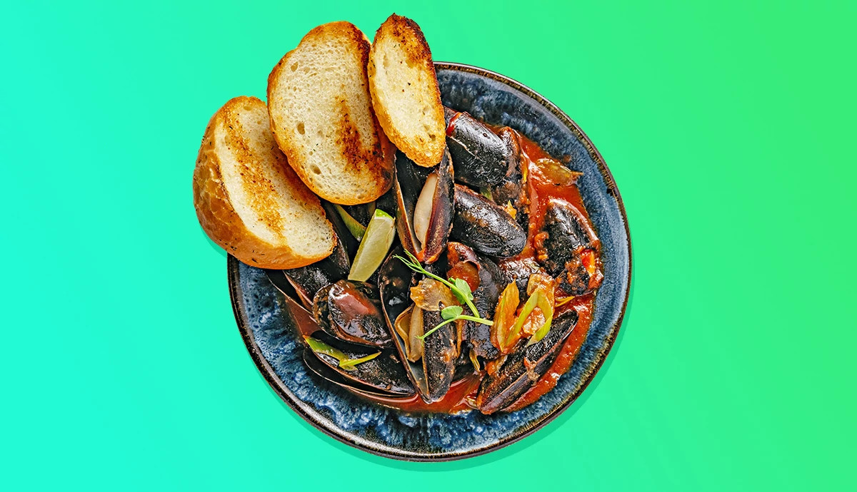 Bowl of steamed mussels in savory red broth with toasted bread slices.