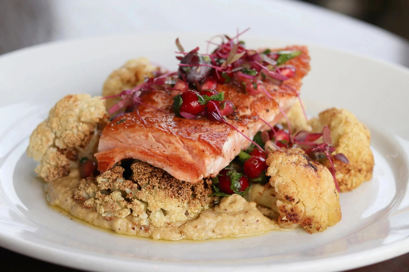 Seared salmon topped with cranberries and microgreens served over roasted cauliflower