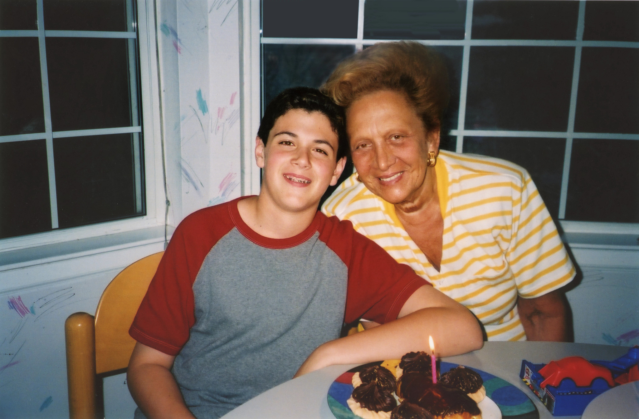 daniel and his grandmother smile in front of cupcakes with a birthday candle