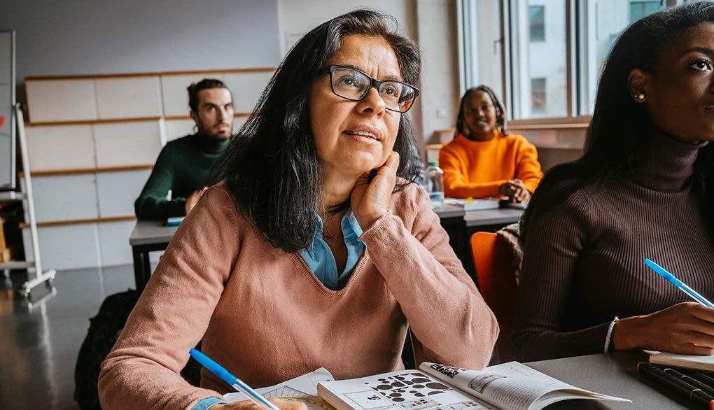 Committing to lifelong learning helps keep your mind engaged A woman taking notes in an adult education class with other students