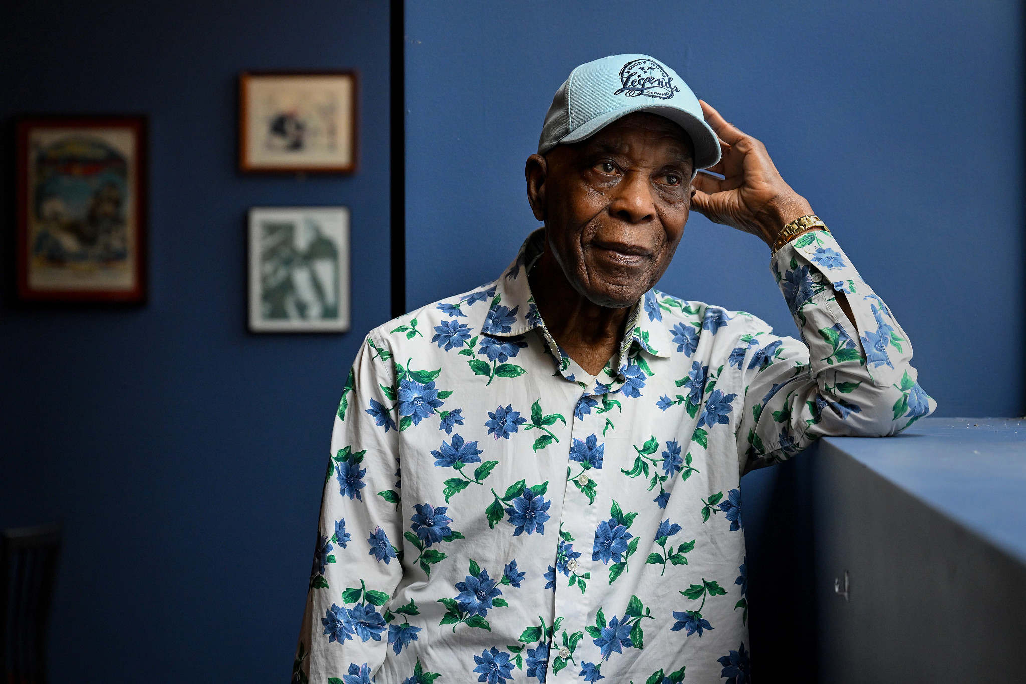 buddy guy posing for a portrait wearing a blue and white floral patterned shirt and a baseball cap