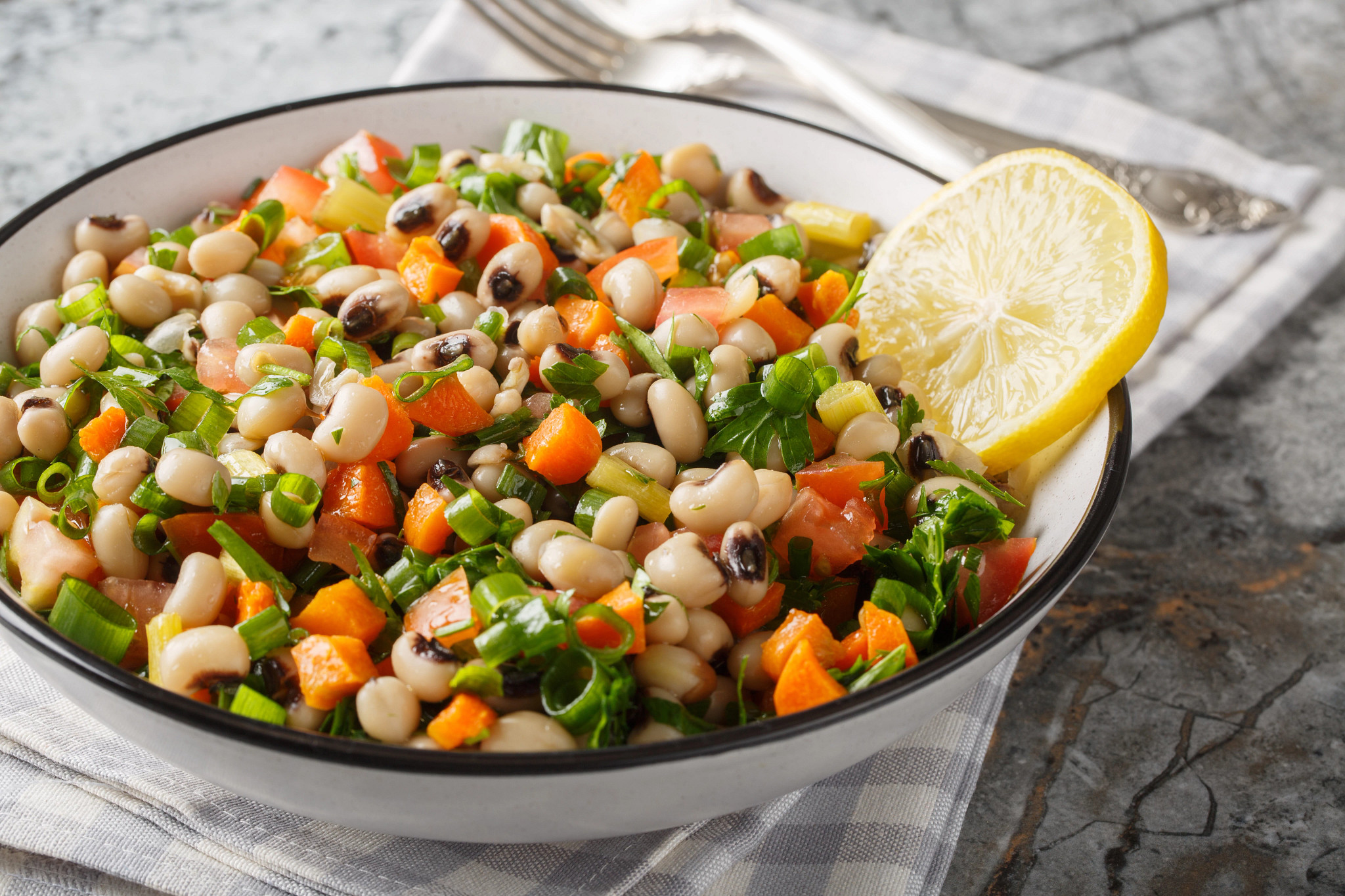 A close-up view of a salad with black-eyed beans, carrots, onions, tomatoes, basil and parsley