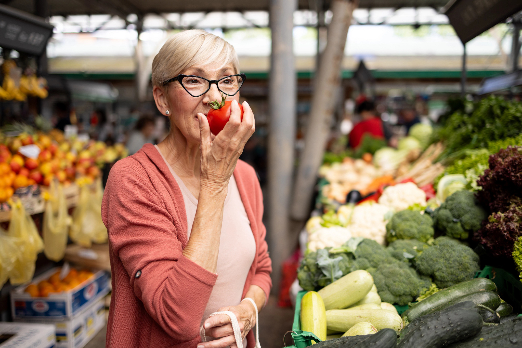 A woman smelling a tomato in her hand at a farmers market
