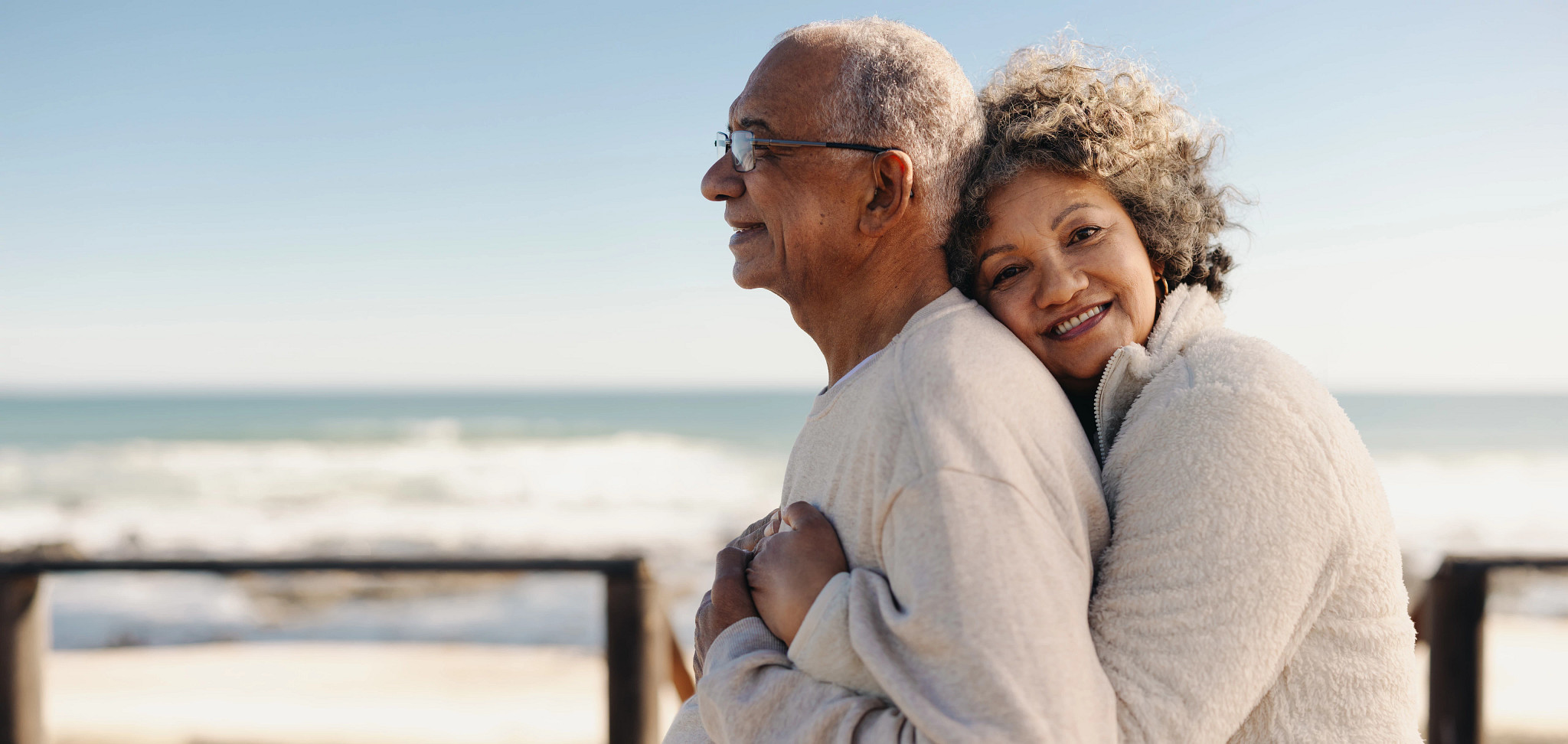 a woman hugging a man from behind on a beach