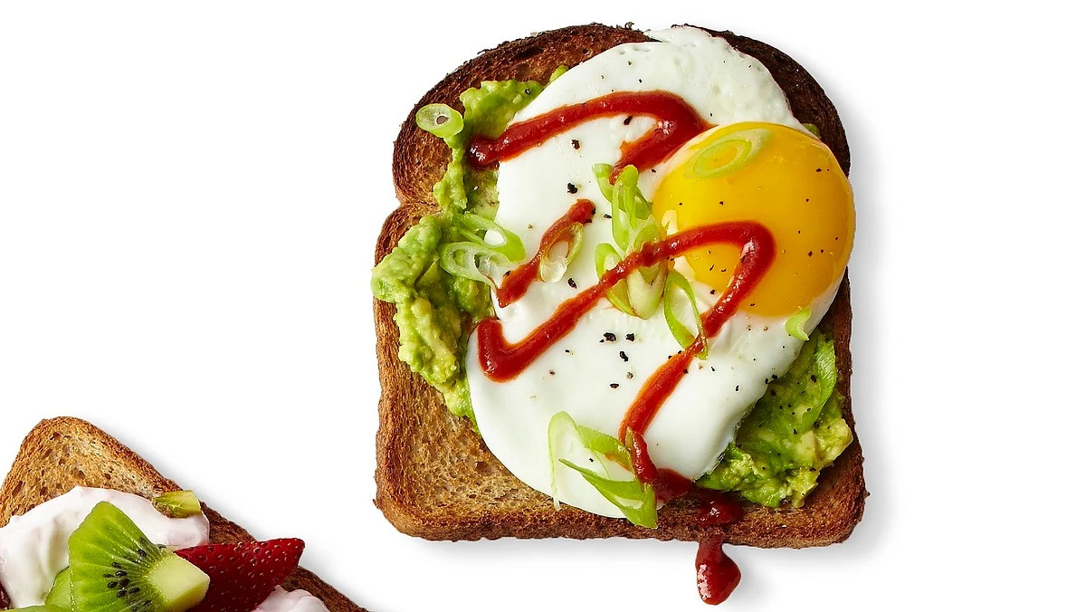 An overhead view of avocado-egg toast on a white background