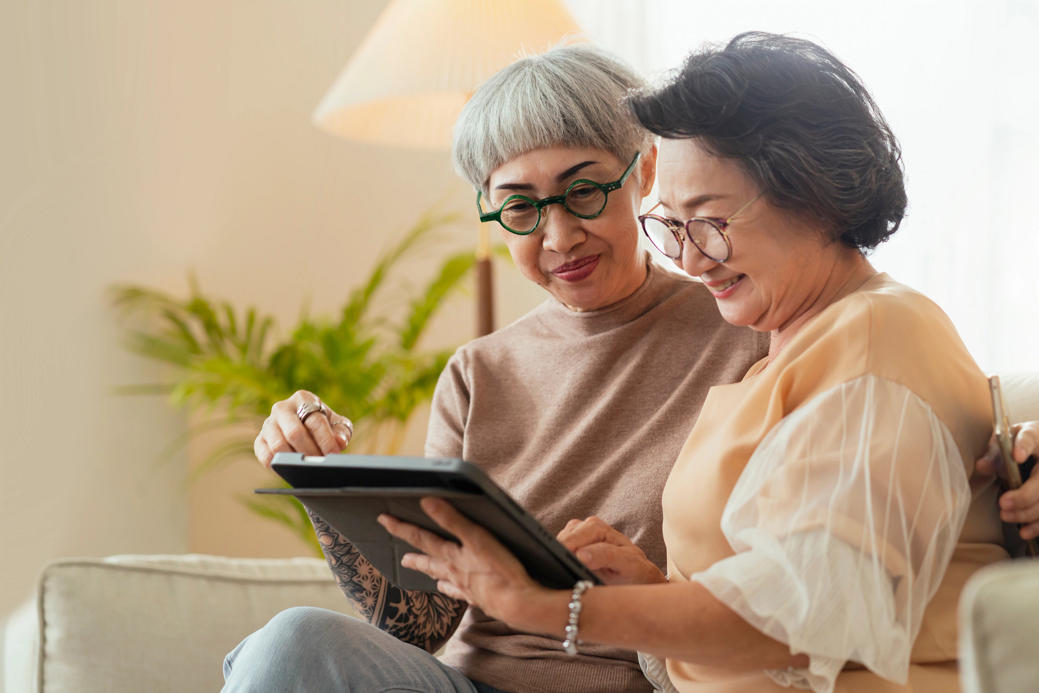 Two senior female friends looking through old photos digital album together with tablet device