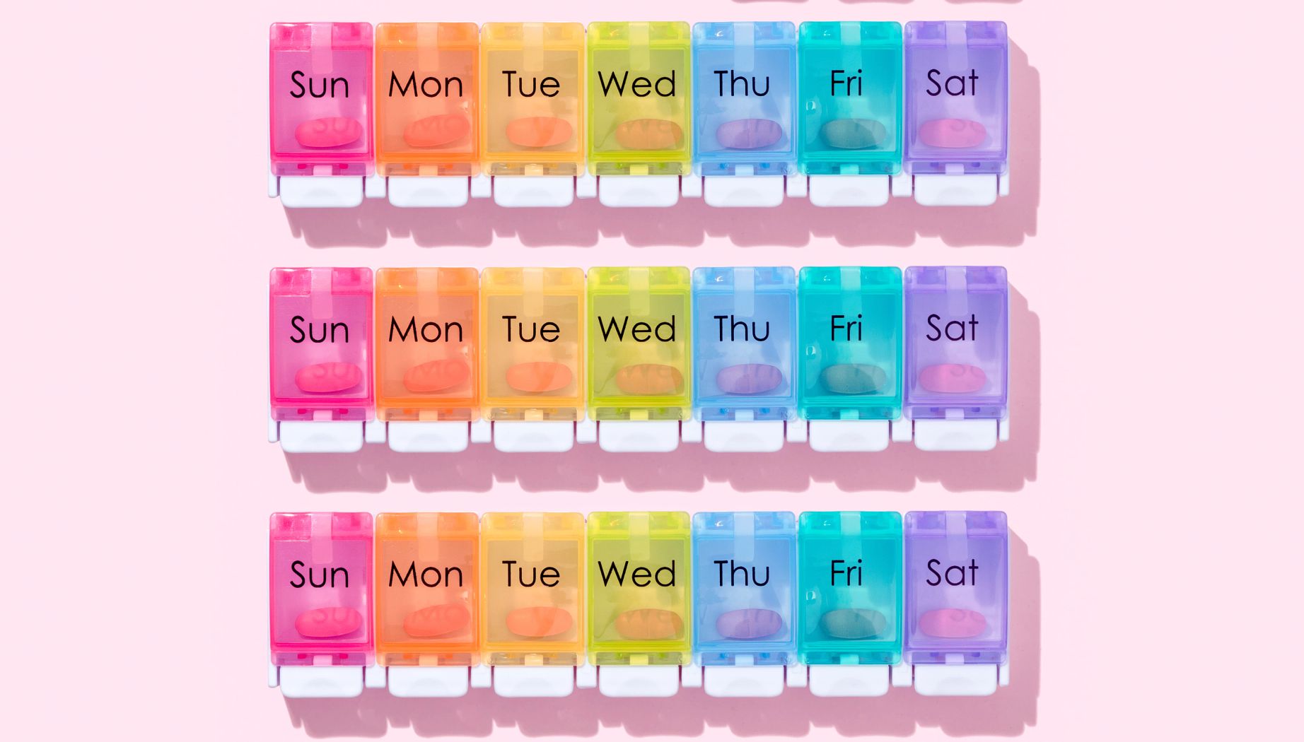 Pill organizer arranged by one calendar month on pink colored background.