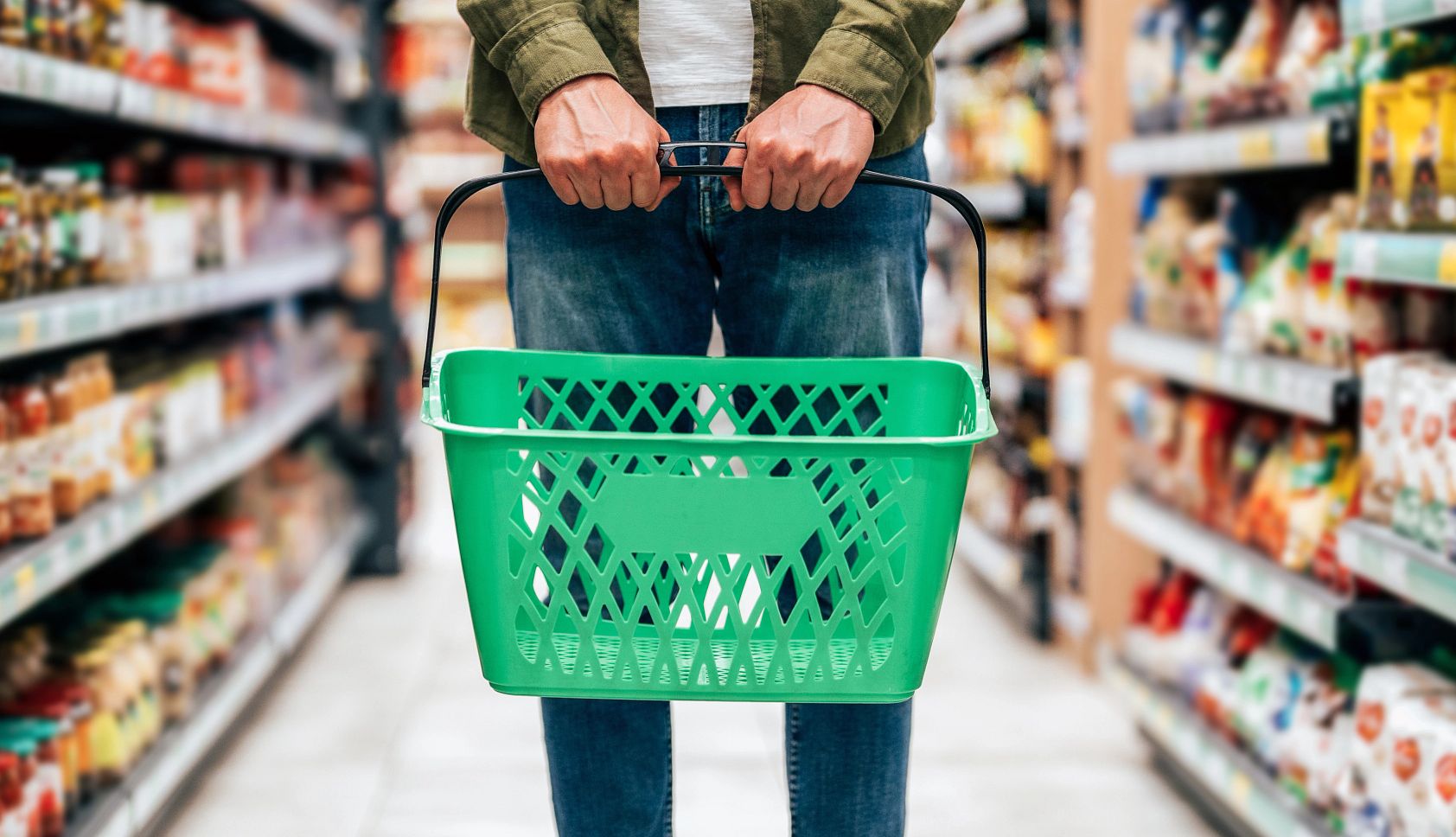 Los recortes a la asistencia alimentaria para adultos mayores son inminentes ante el avance del proyecto de ley ‘One Big, Beautiful Bill Act’ foto de la mitad de un cuerpo humano agarrando una canasta de mercado vacía. Persona parada en un pasillo de supermercado lleno.