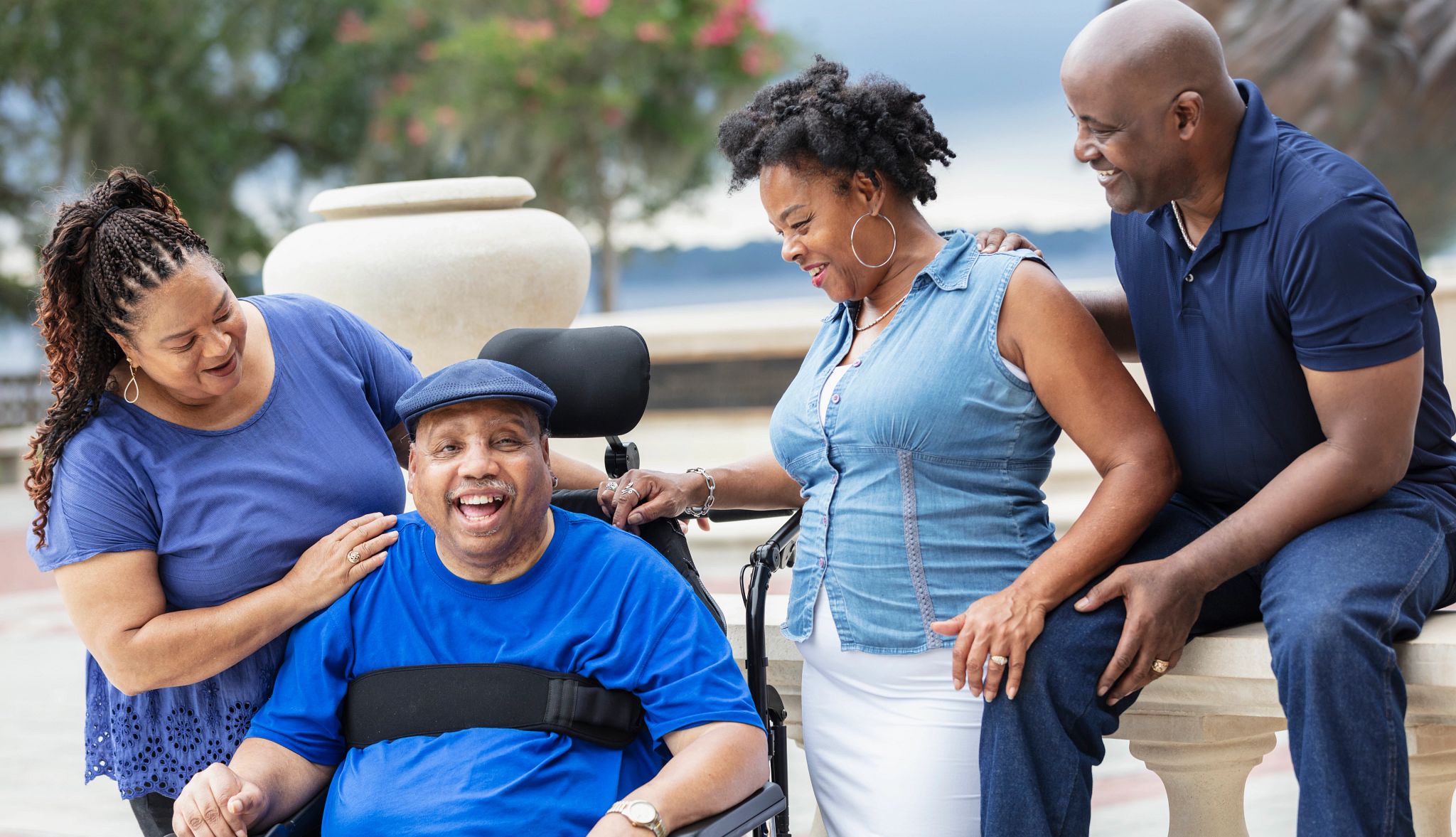A group of four senior African-American friends, two couples, hanging out at a city park. One of the men is in a wheelchair from a physical disability due to an accident. He is smiling at the camera. A group of four senior African-American friends, two couples, hanging out at a city park. One of the men is in a wheelchair from a physical disability due to an accident. He is smiling at the camera.