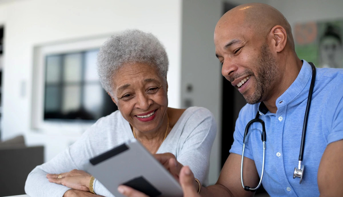 A doctor of color smiles while helping an older female patient.