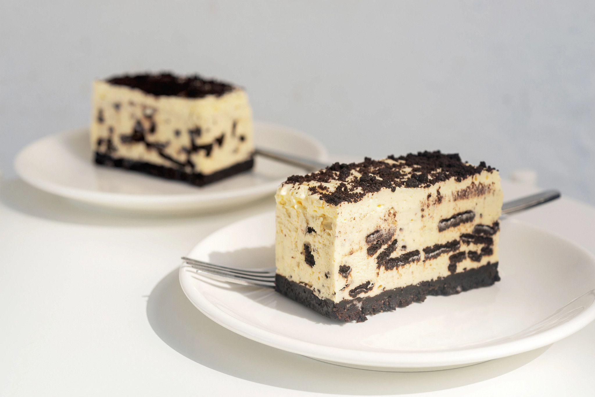 Close-up photo of Oreo Cheesecake Bars featuring layers of cream filling and chocolate cookie crumbs on white plates
