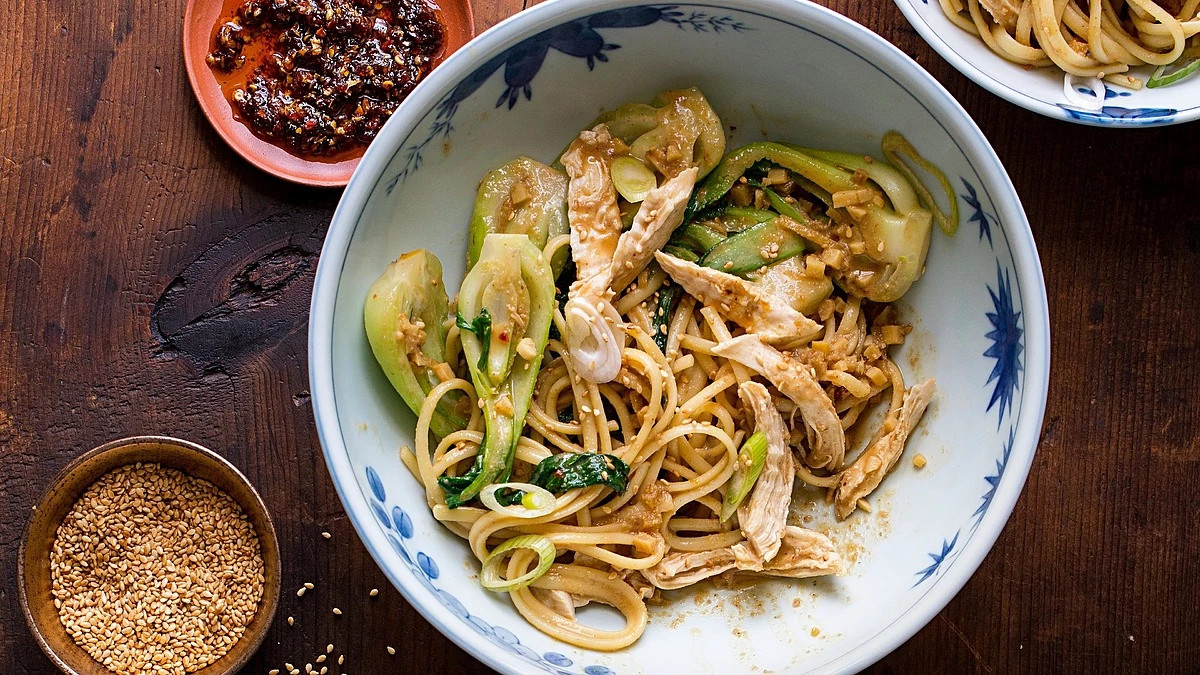 A close-up view of dan dan noodles with chicken and bok choy in a bowl