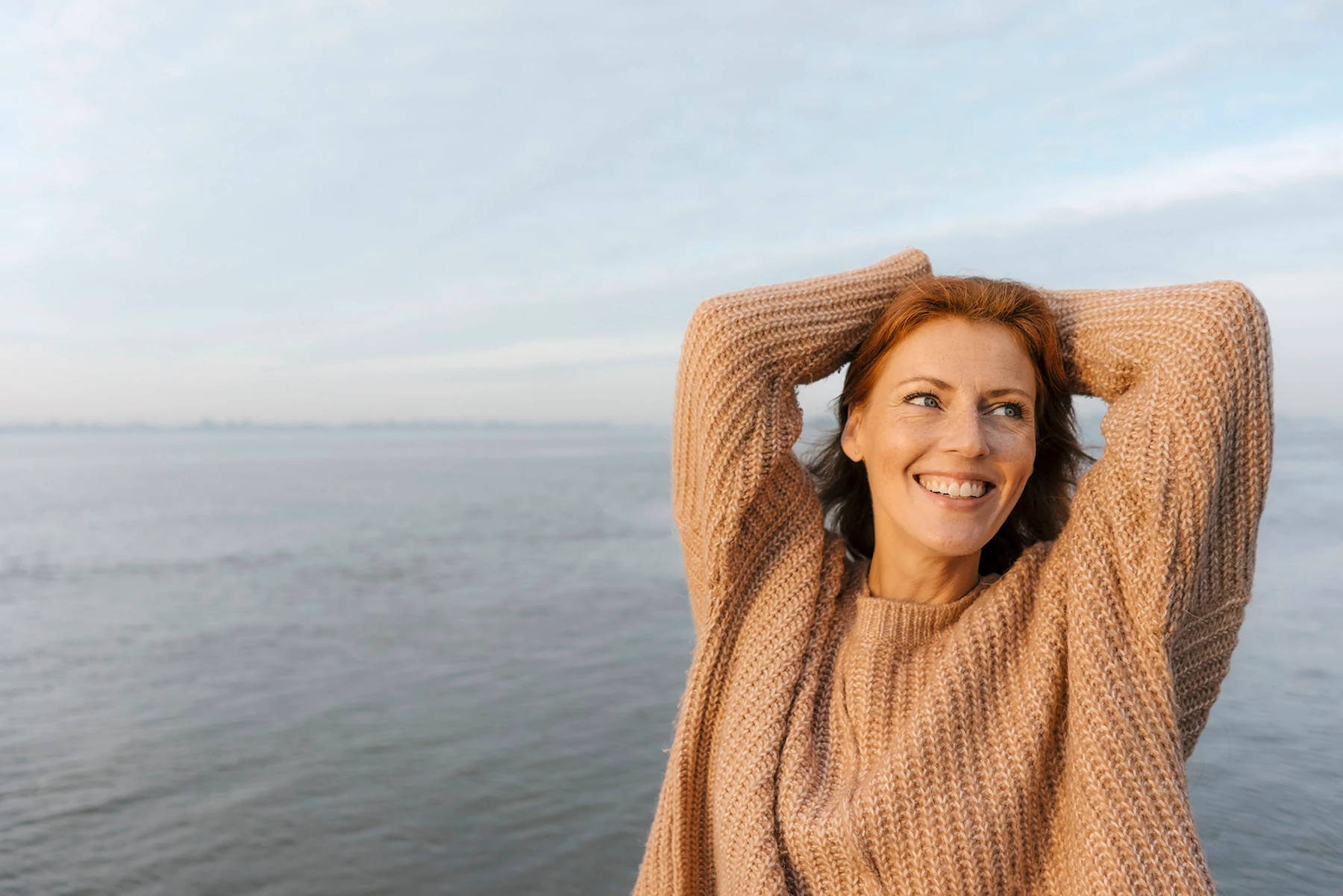 happy woman in her 40s by the water in a sweater