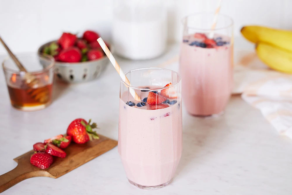 Pink berry smoothie topped with fresh strawberries and blueberries on a marble counter