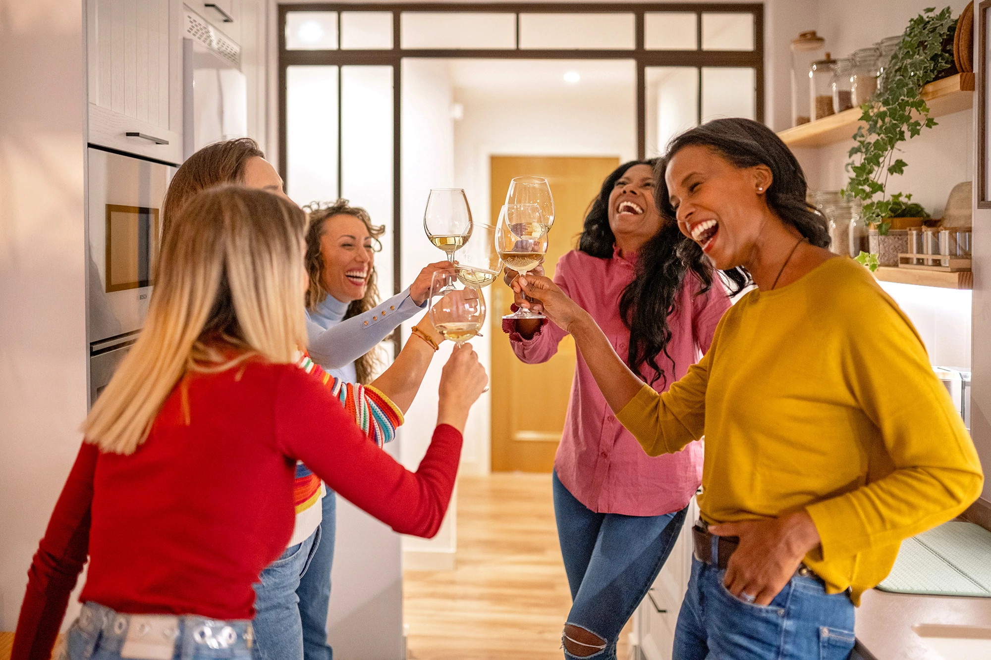 Four women standing close together with arms around each other, smiling and dressed in colorful outfits. The background is pink and beige with decorative stars and sparkle illustrations. At the top, a logo features eyeglasses with the words “The Ethel” and the tagline “An AARP Community.”
