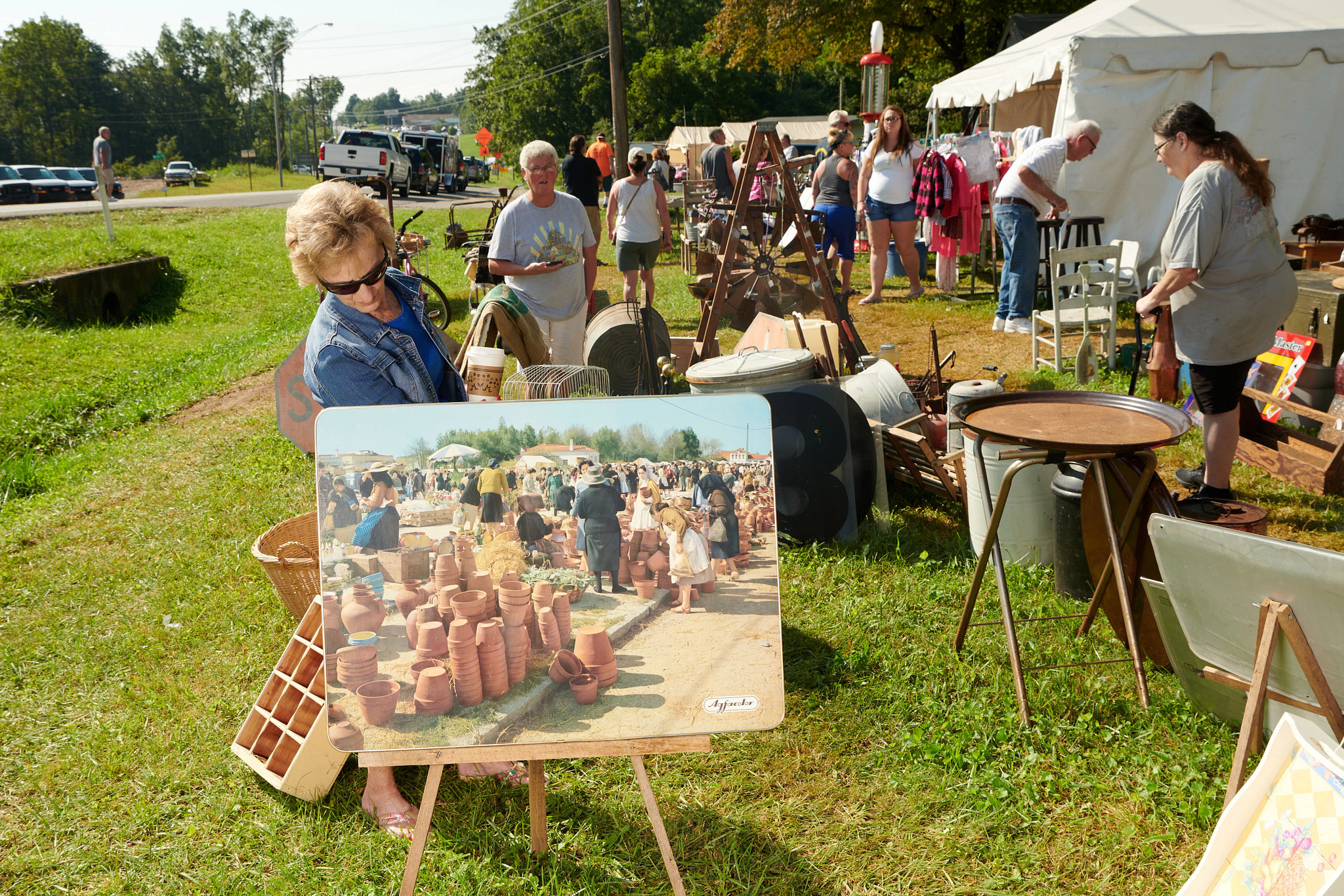 a woman looking at a painting at a yard sale