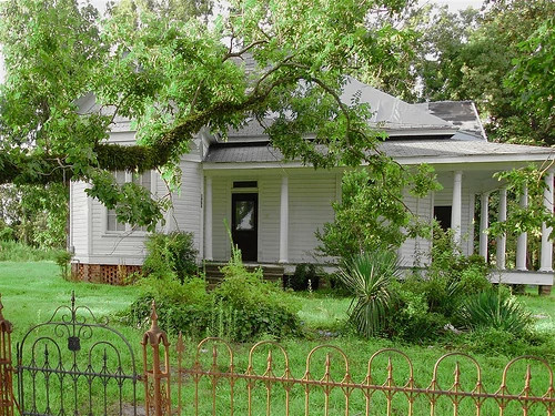 A white, single-story house with a large wraparound porch and white columns