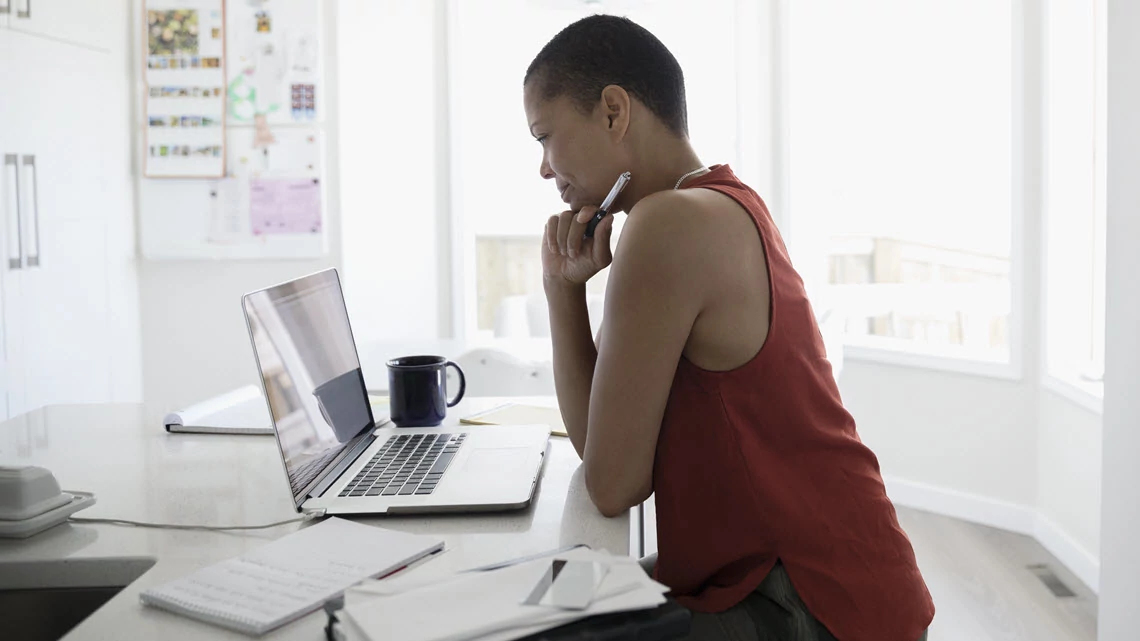 woman looking at the computer with papers around her and pen in hand