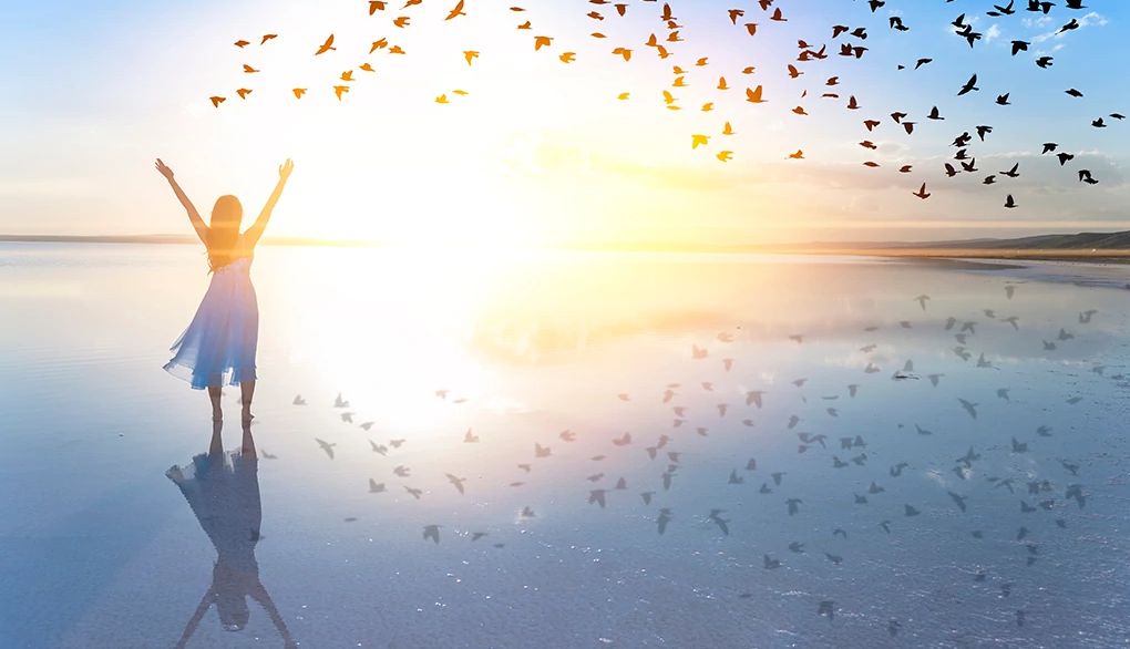 Setting attainable goals may improve mental health and quality of life A woman with her arms raised standing by a lake at sunset