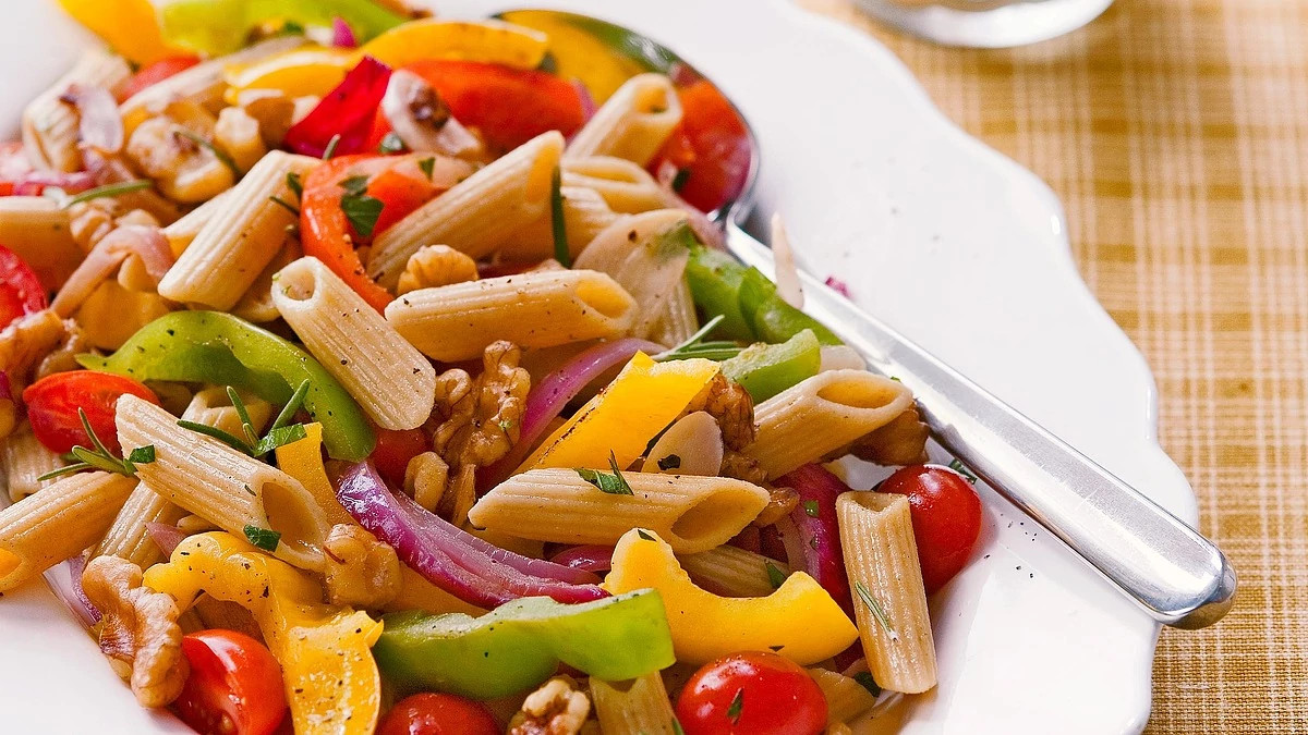 A close-up view of penne with walnuts and peppers on a plate
