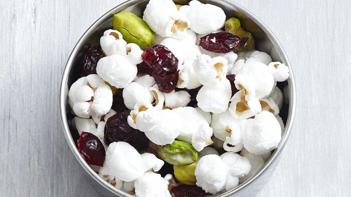 A close-up view of fruit and nut popcorn trail mix in a bowl