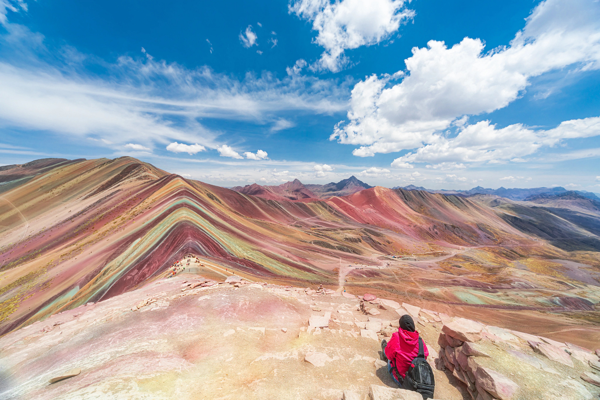 Una persona está sentada frente a dunas montañosas multicolores.