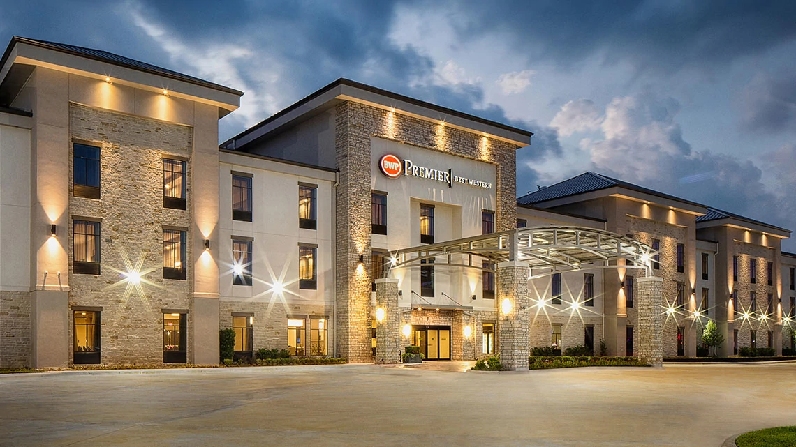 Front of hotel at night with lights on outside, covered front entrance, beige, brick siding