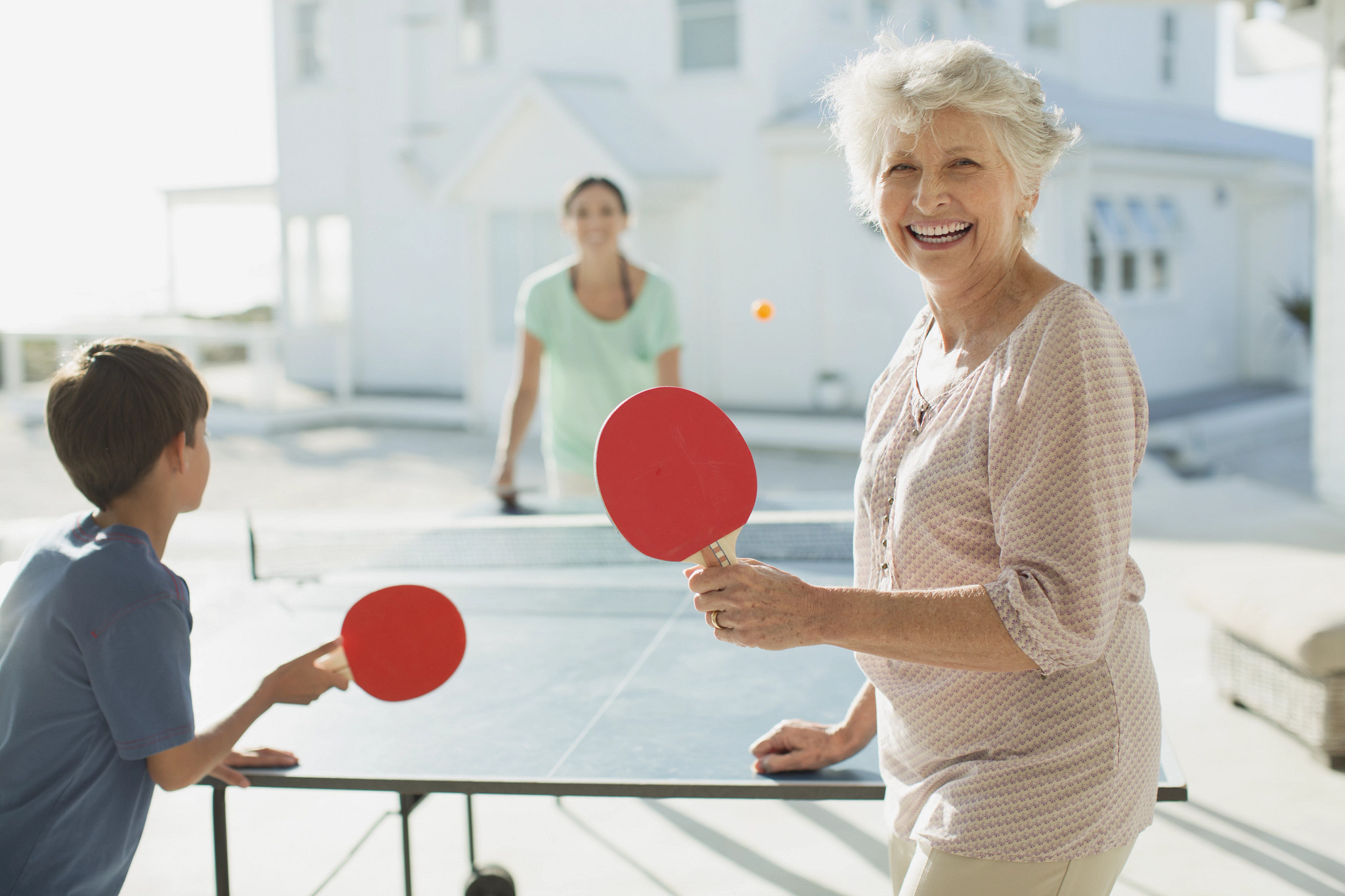 Multi-generation family playing table tennis outside beach house