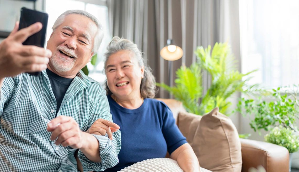 AARP Navigator Making the Most of Medicare Mature couple looking at AARP Navigator Medicare resources on their phone while sitting on living room sofa together