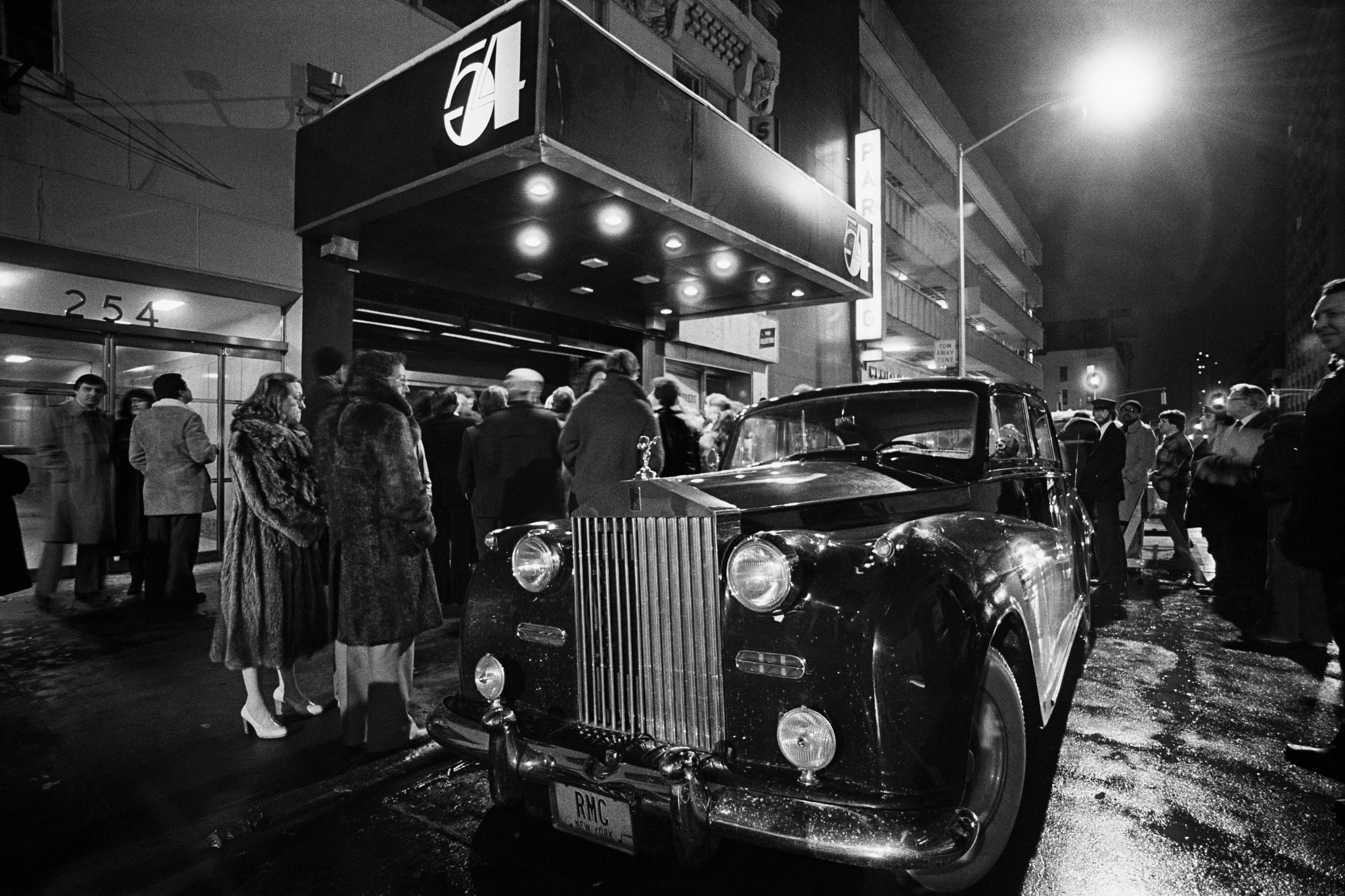 an exterior view of studio 54, with a vintage rolls royce car and a crowd of people waiting to get in