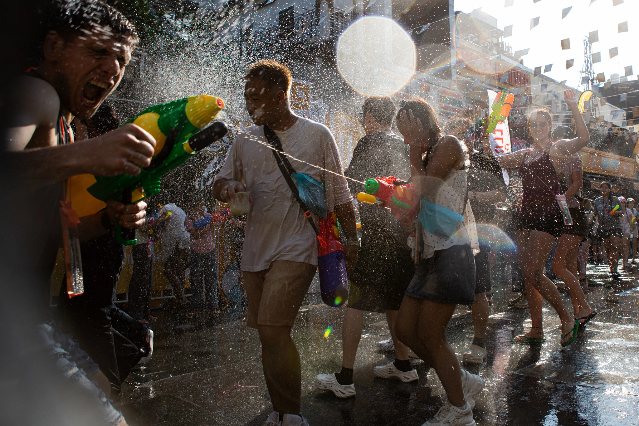 Group of people participating in a lively festival on a sunny city street, spraying water guns and splashing each other during a celebration