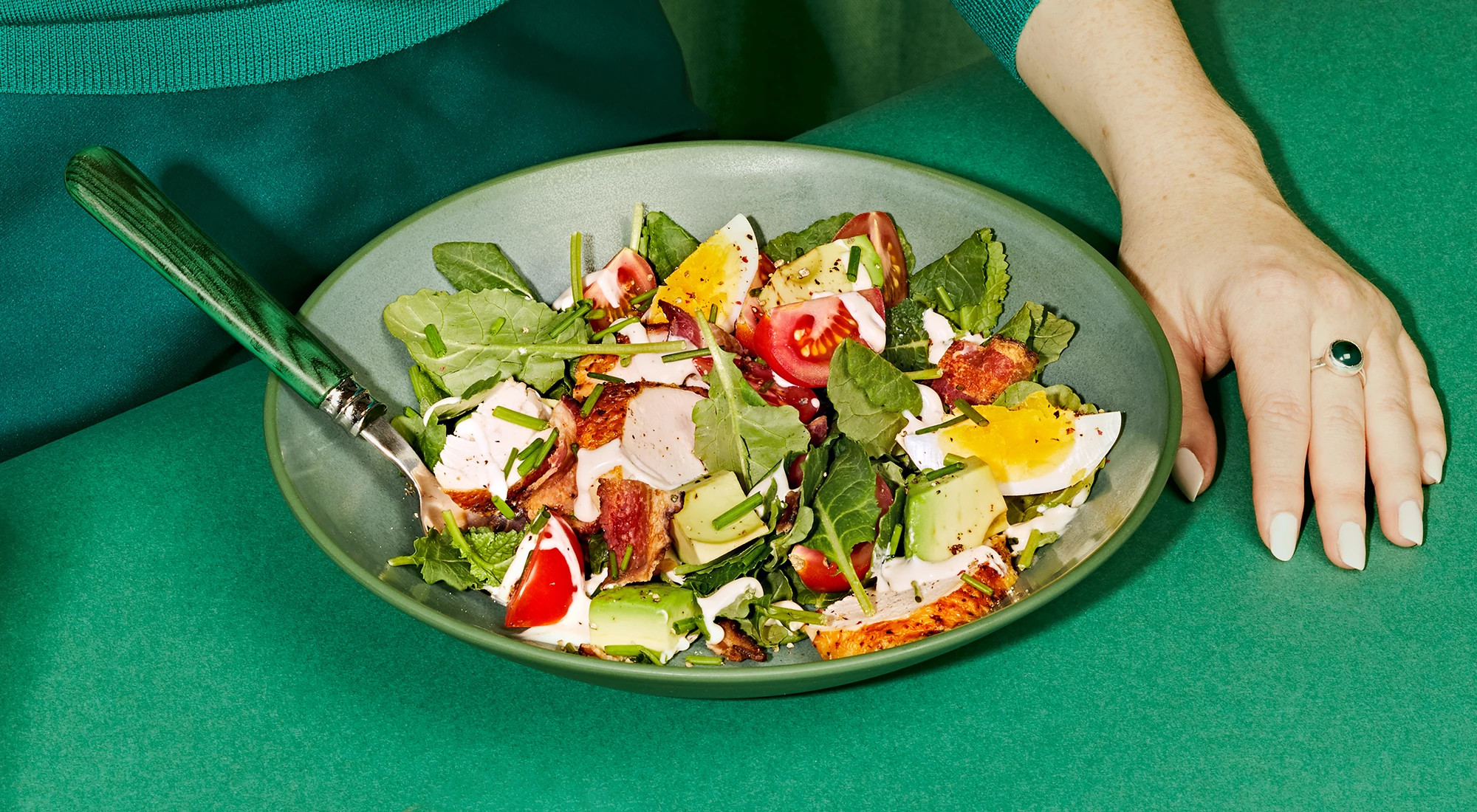 View of salad and woman's hand on a green background