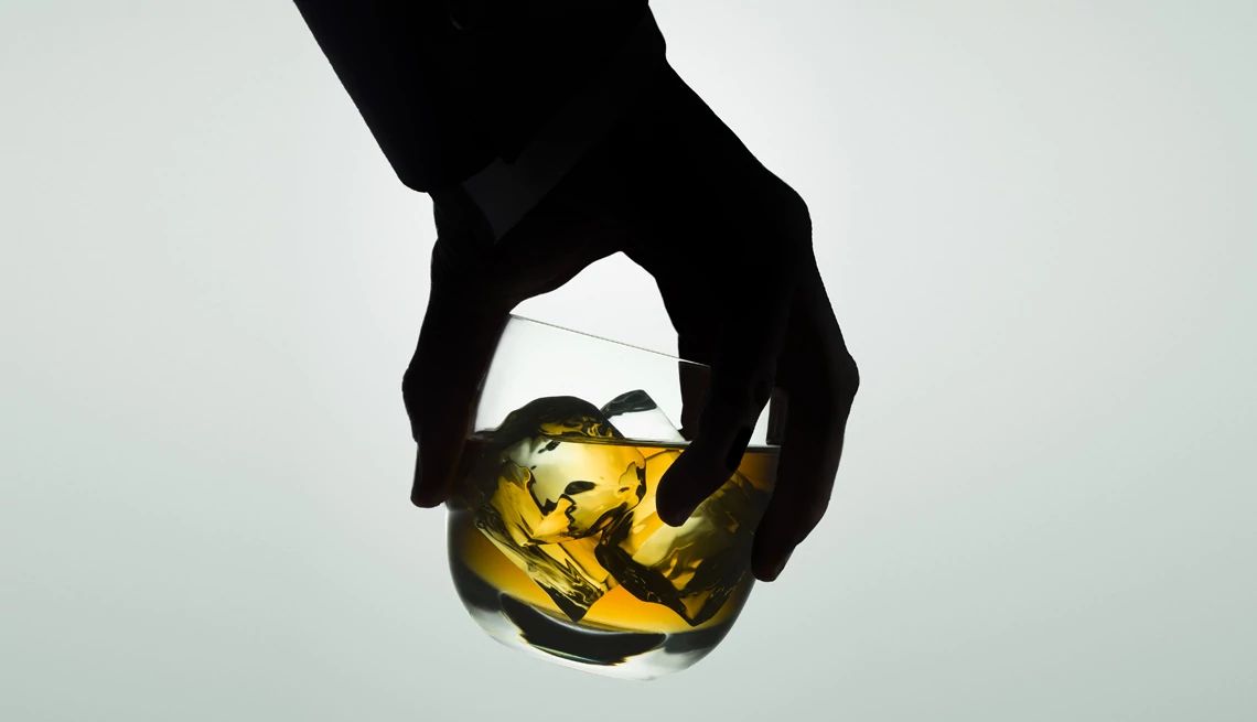 age and alcohol shadow of a hand holding a rocks glass