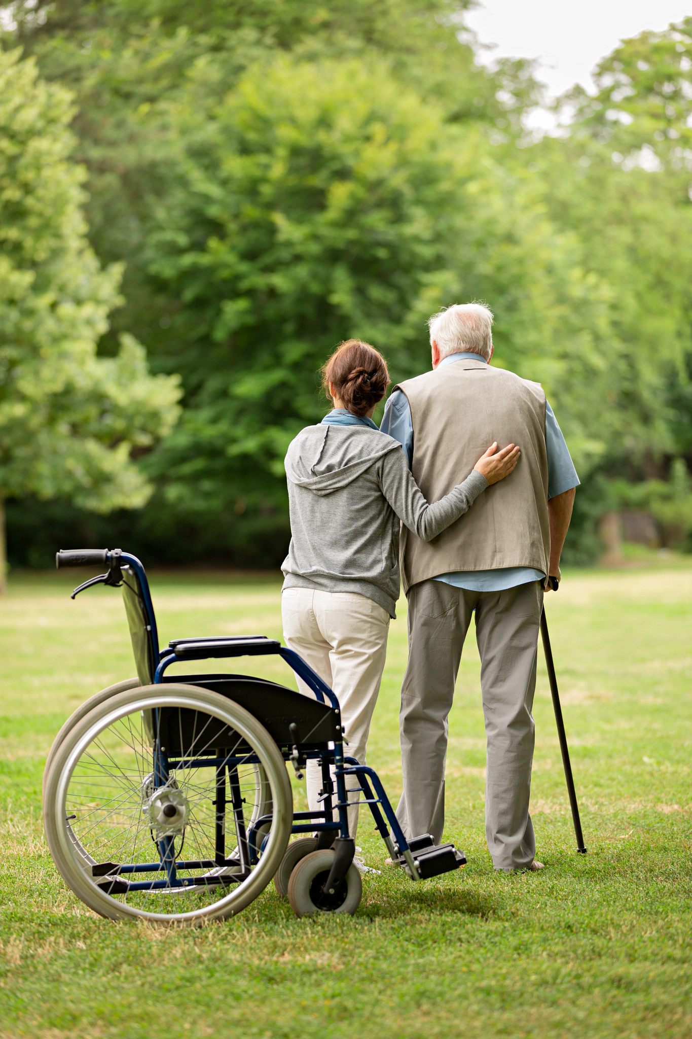 Man standing next to wheelchair with caregiver at the park