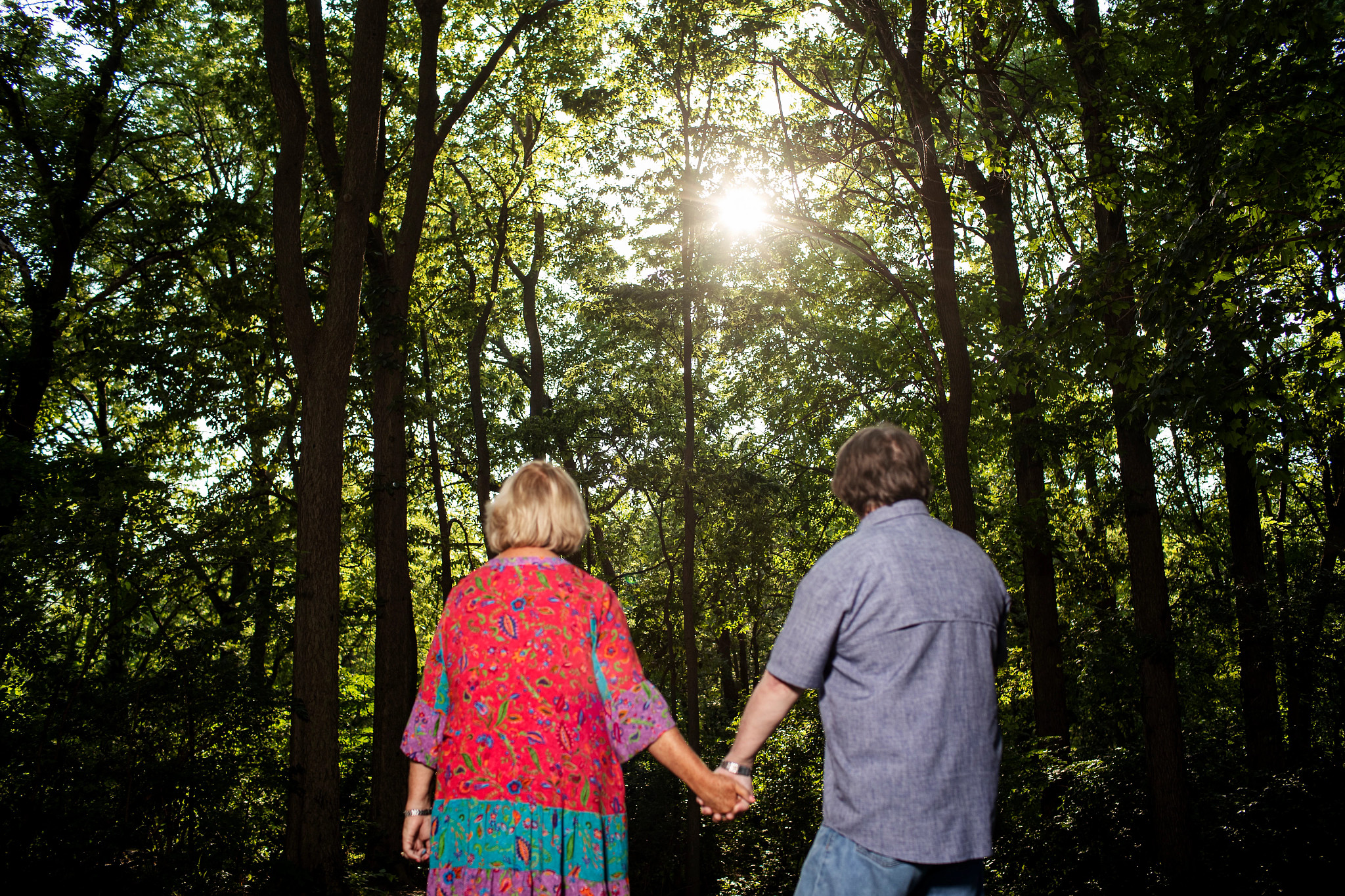 Marty Parrish and Peggy Huppert hold hands and look away from the camera into a wooded area