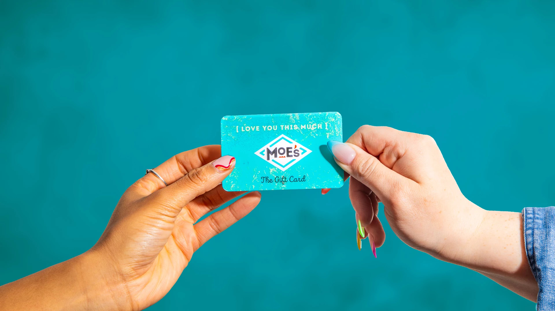 Dos manos sosteniendo una tarjeta de regalo de Moe's Southwest Grill