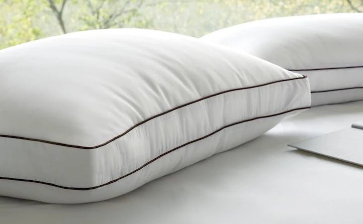 Two Saatva Latex Pillows on a bed in front of a window with trees outside