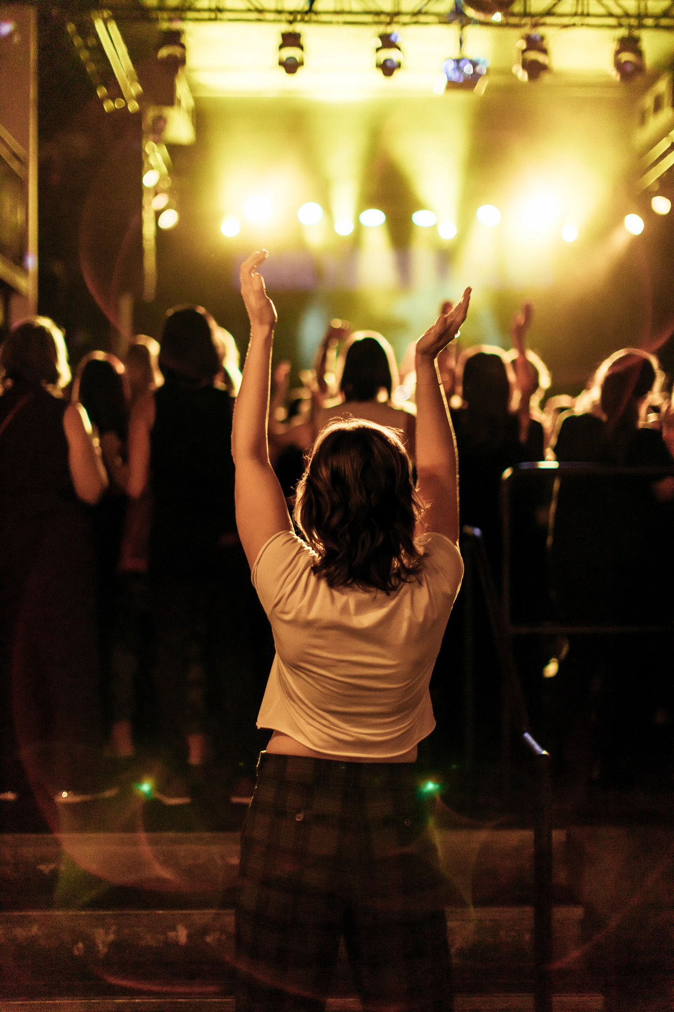 a photo shows Laura Baginski with dancing with her hands raised, behind a full dance floor at an Earlybirds Club dance party