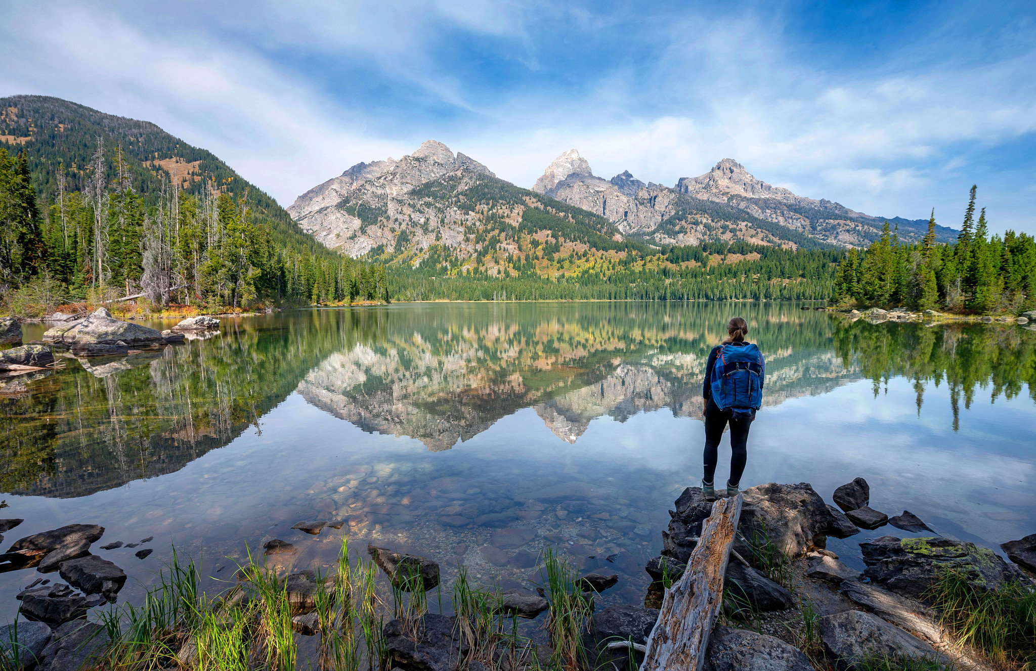 View of woman from behind with the Grand Teton Mountains in the distance reflecting in a lake