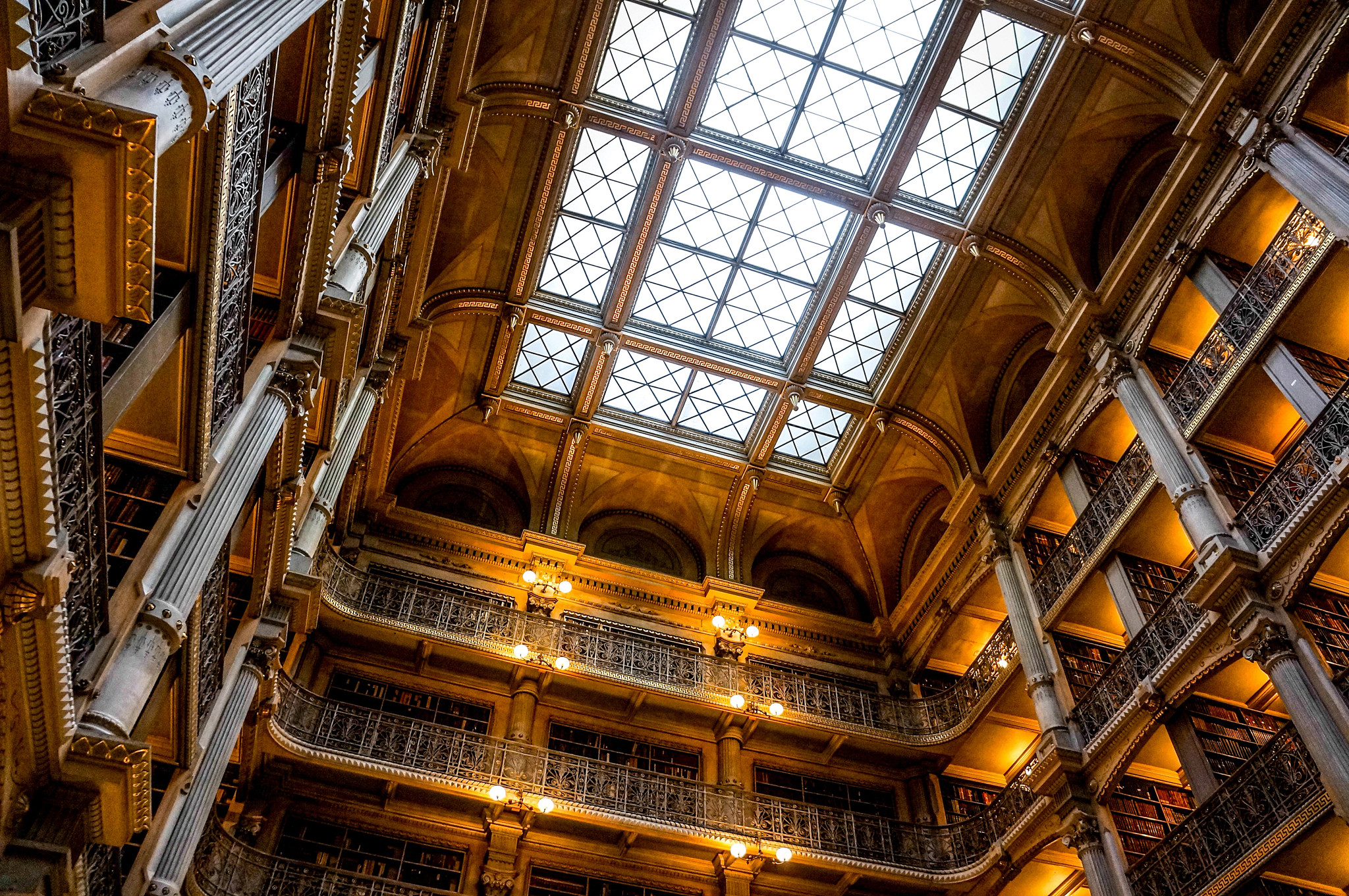 Historic library interior with multiple levels of bookshelves, decorative iron railings, columns and a large glass skylight.