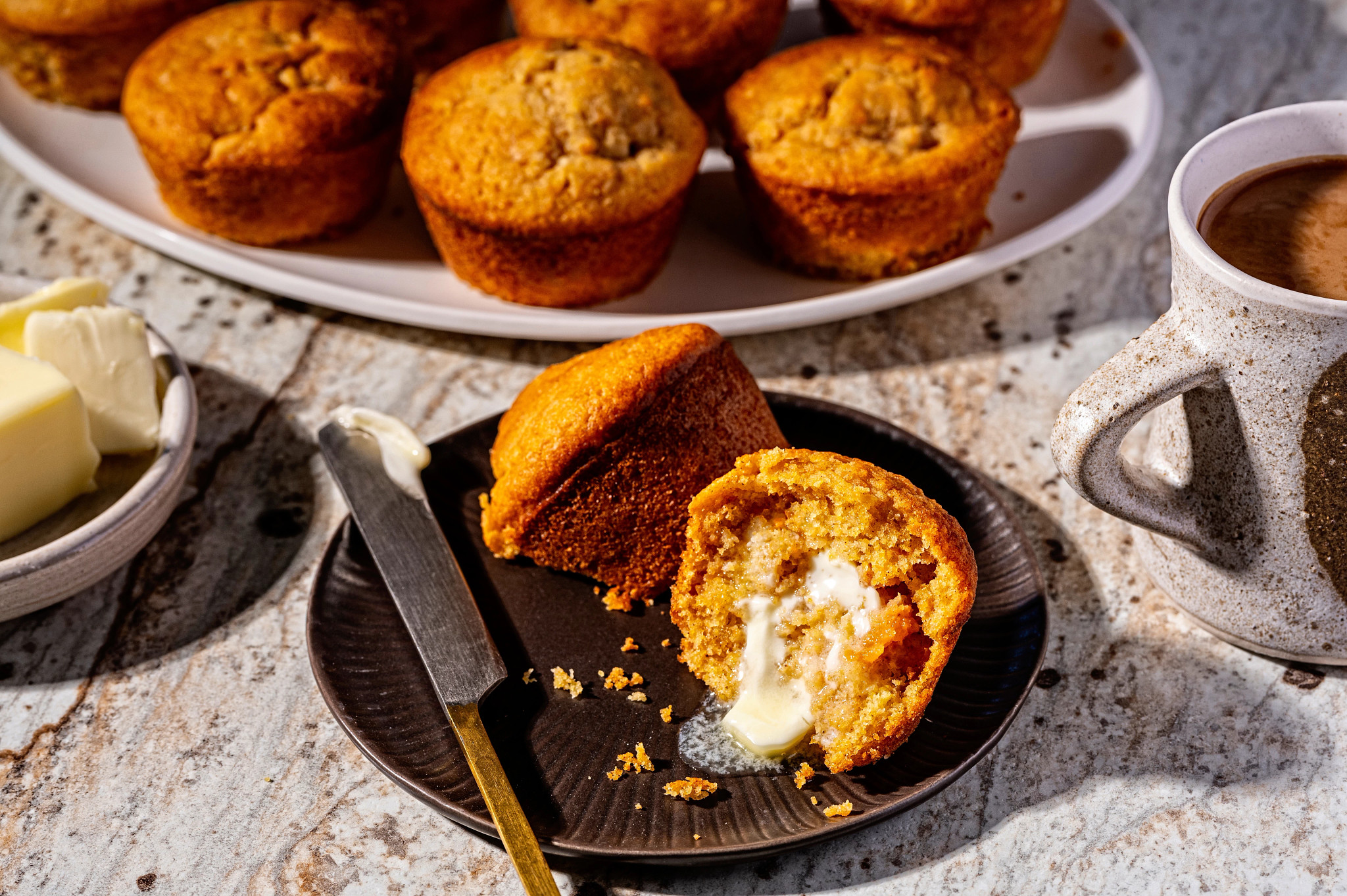 mashed sweet potato muffins are shown in a photo, with one on small gray plate, split open with butter spread onto it