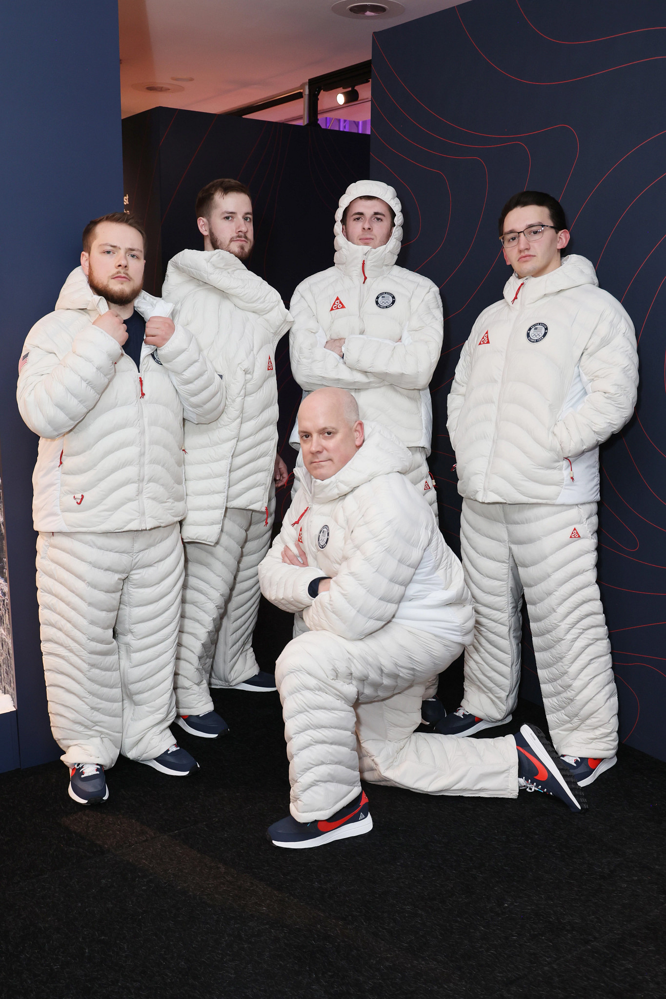Rich Ruohonen kneels in the foreground surrounded by the four younger members of the U.S. Olympic men’s curling team, all wearing white Team USA puffer suits.