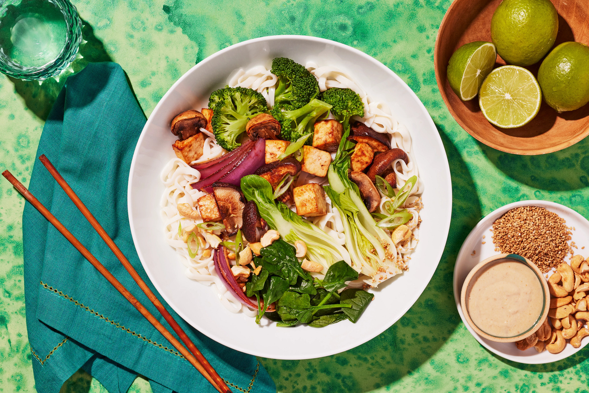 Plant-based noodle bowl with broccoli, tofu, mushrooms, greens, chopsticks and fresh limes
