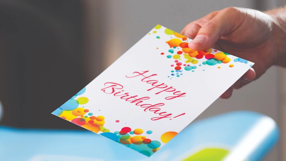 hand holding a happy birthday card with blue, red, orange, yellow colored circles scattered on the card with happy birthday in red and cursive