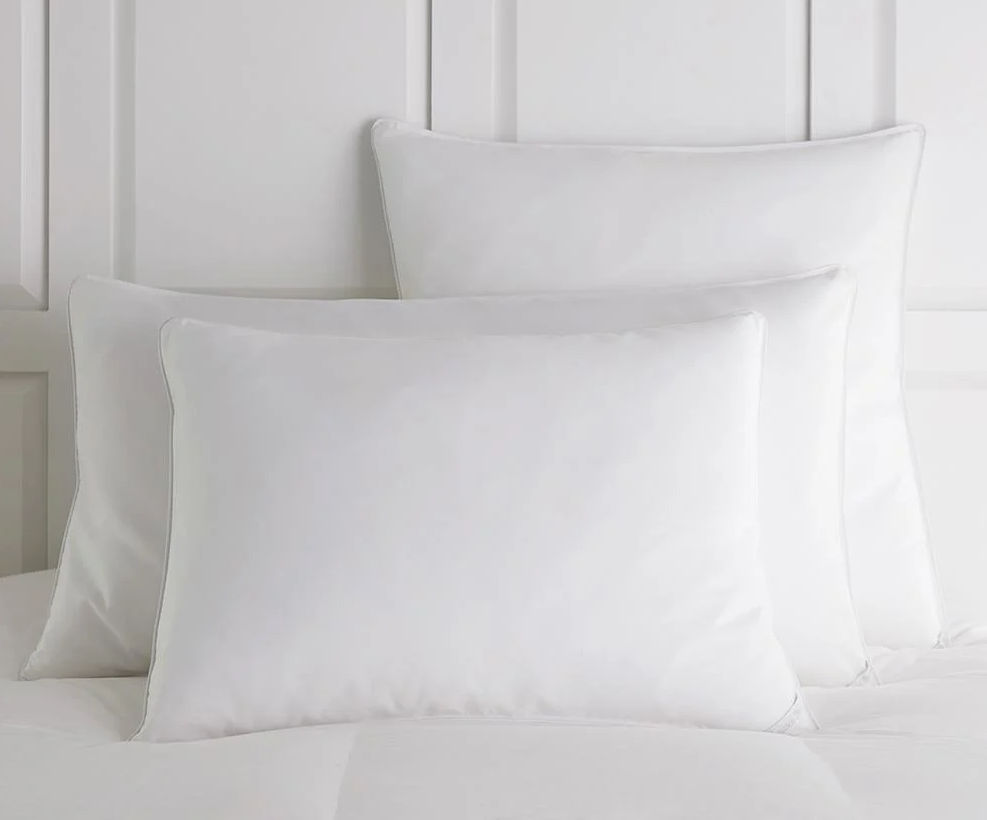 Three Peacock Alley Down Alternative Pillows stacked on a white bed and against a white wall.