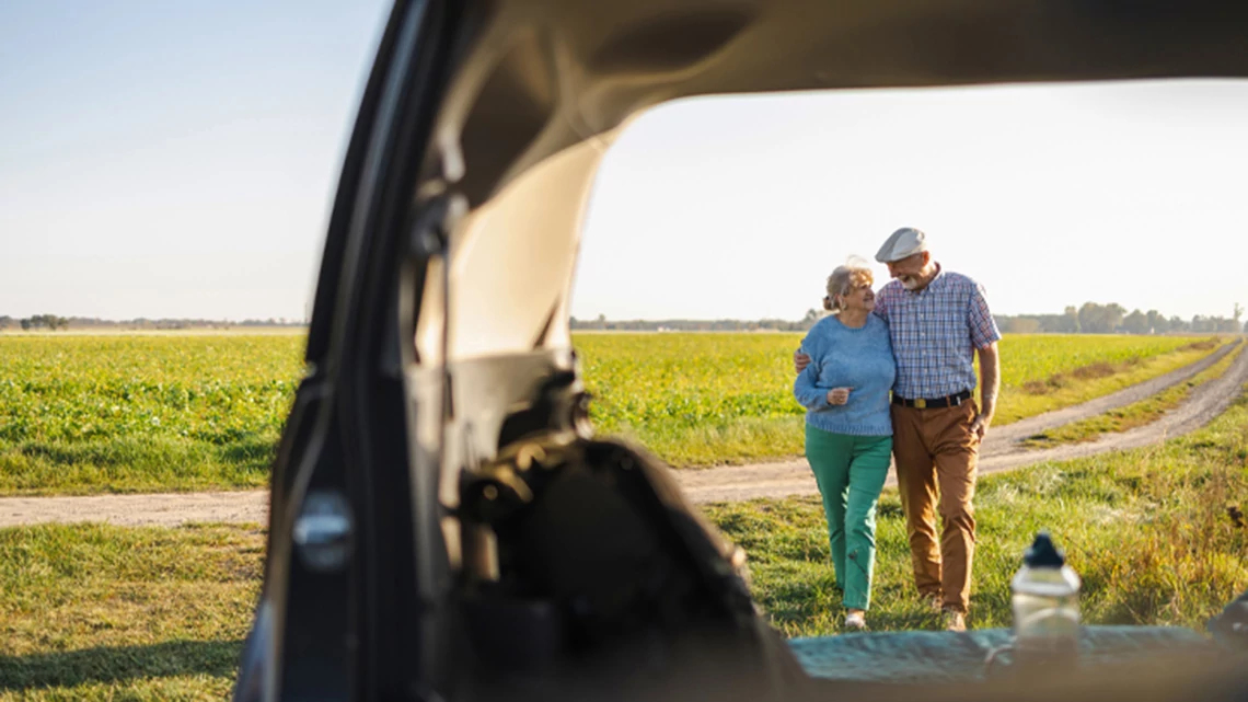 Mature couple hugging and walking through a field on vacation with view from an SUV trunk