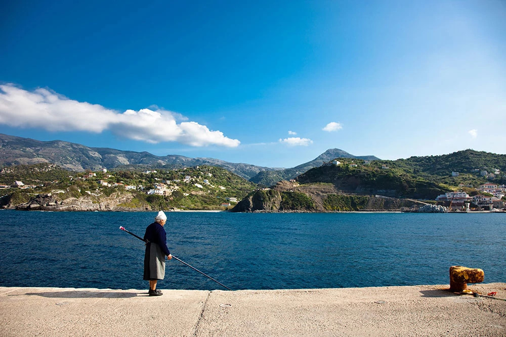 Woman walks along the water in Ikaria, Greece.