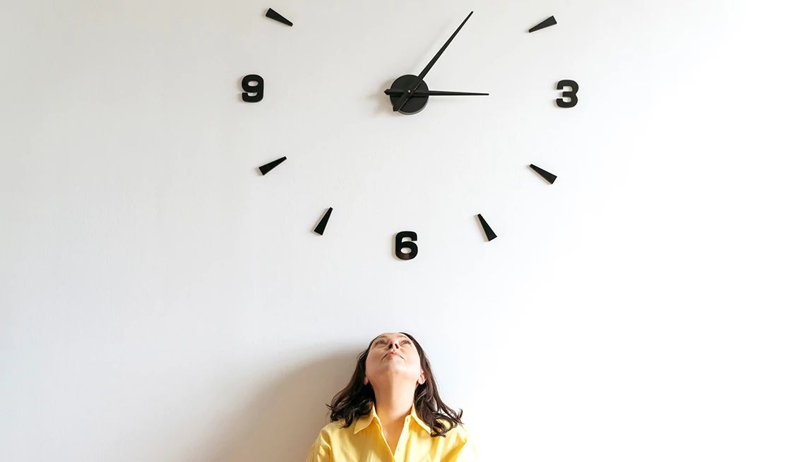 Descubre cómo es la jubilación temprana Una mujer mirando un reloj sobre una pared blanca